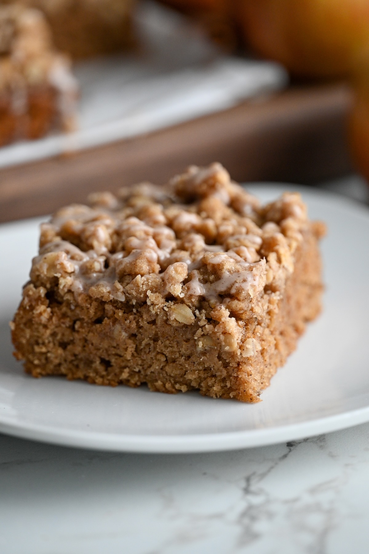 close up view of sliced applesauce coffee crumb cake on a white plate with the rest of the cake in the background.