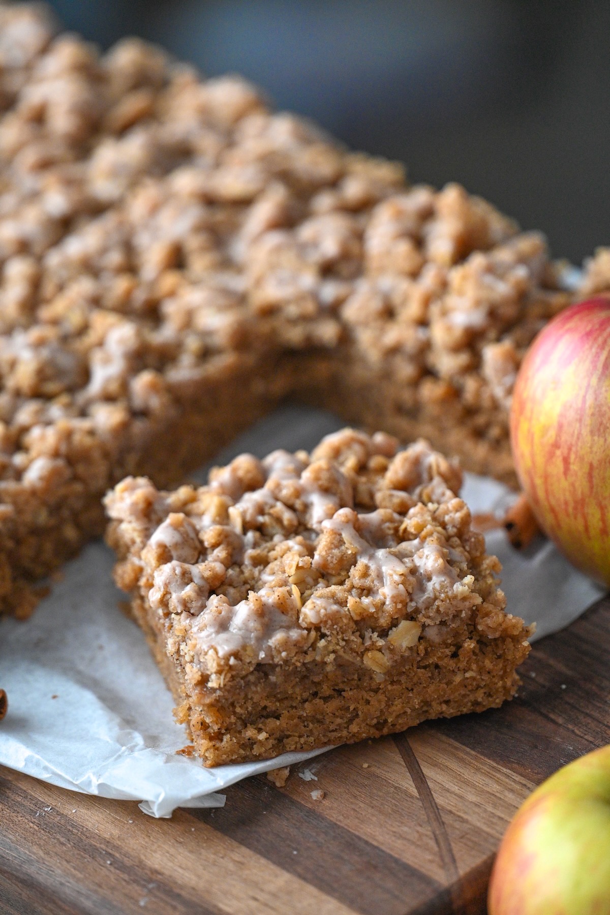 sliced piece of homemade applesauce crumb coffee cake on parchment next to fresh apples and the remaining cake.