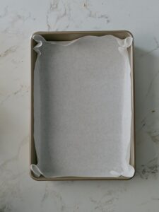 A rectangular cake pan lined neatly with parchment paper.