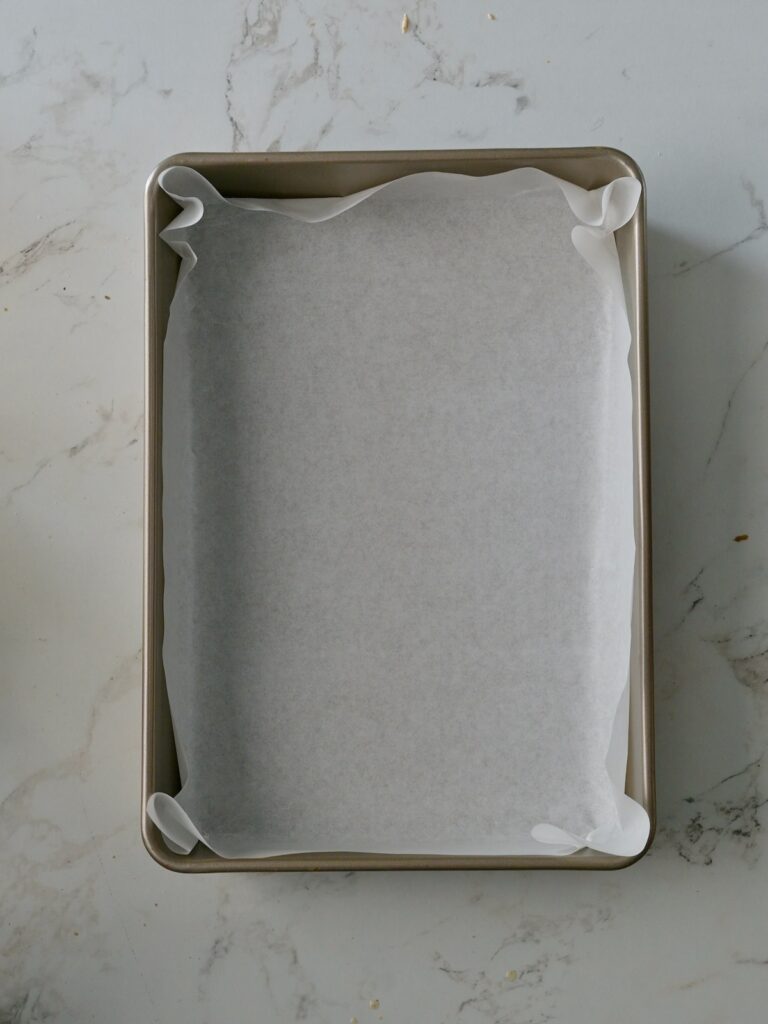 A rectangular cake pan lined neatly with parchment paper.