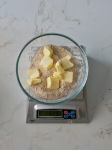 Cubes of butter sitting on top of a bowl of flour, sugar, and cinnamon mixture, ready to be mixed into a crumb topping.