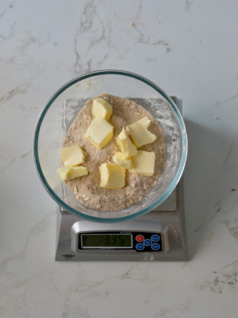 Cubes of butter sitting on top of a bowl of flour, sugar, and cinnamon mixture, ready to be mixed into a crumb topping.