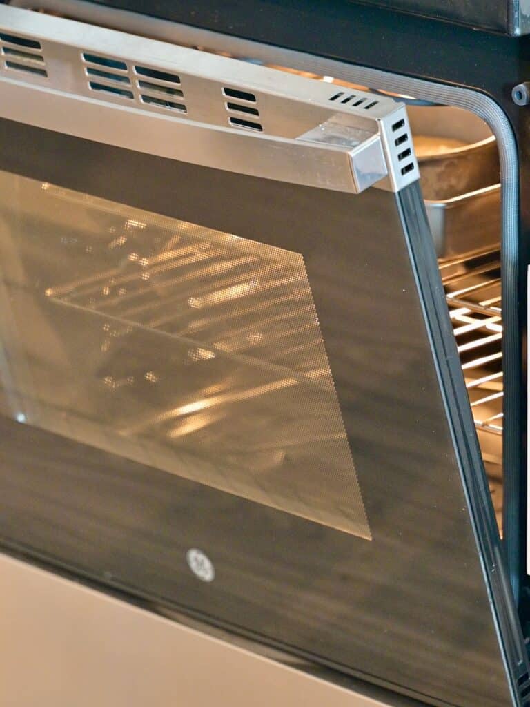 Cheesecake baking in a water bath inside an oven with the door propped slightly open to cool slowly and prevent cracks.