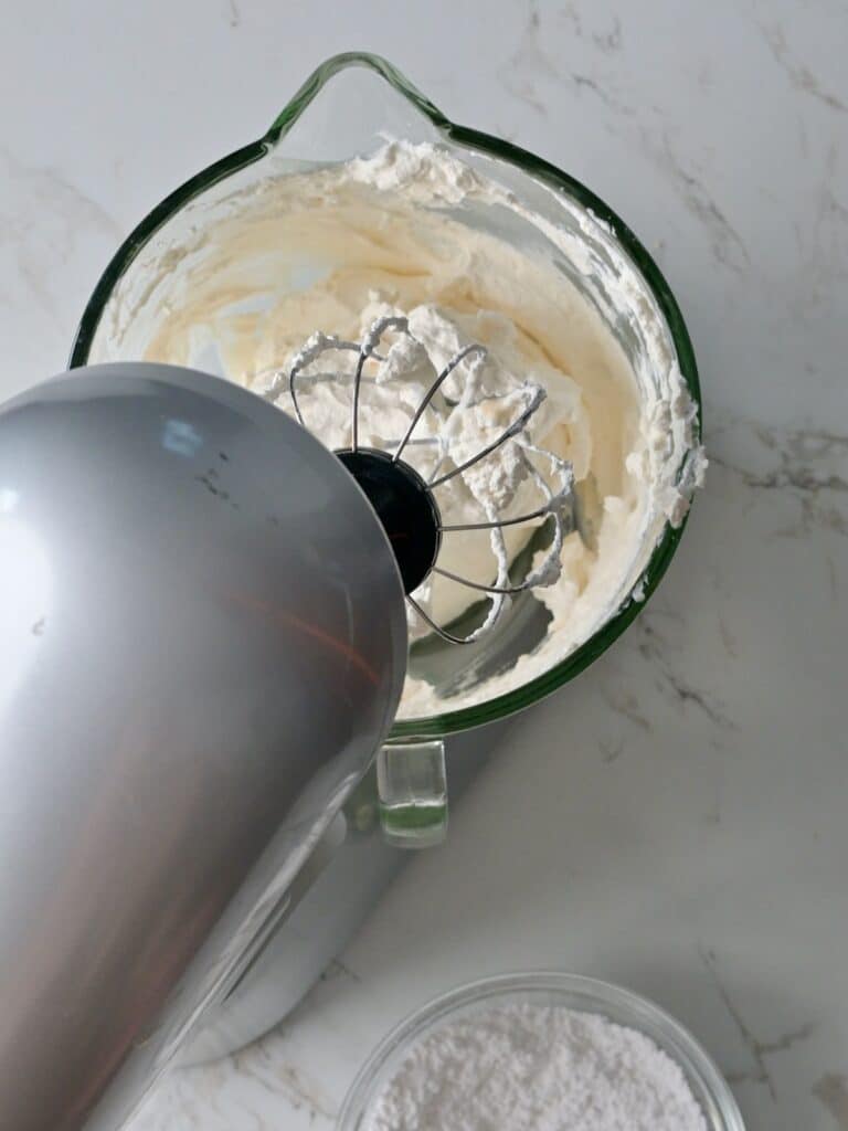 Fresh whipped cream being whipped in a stand mixer with a wire whisk attachment until thick and fluffy for the pumpkin mousse and frosting.