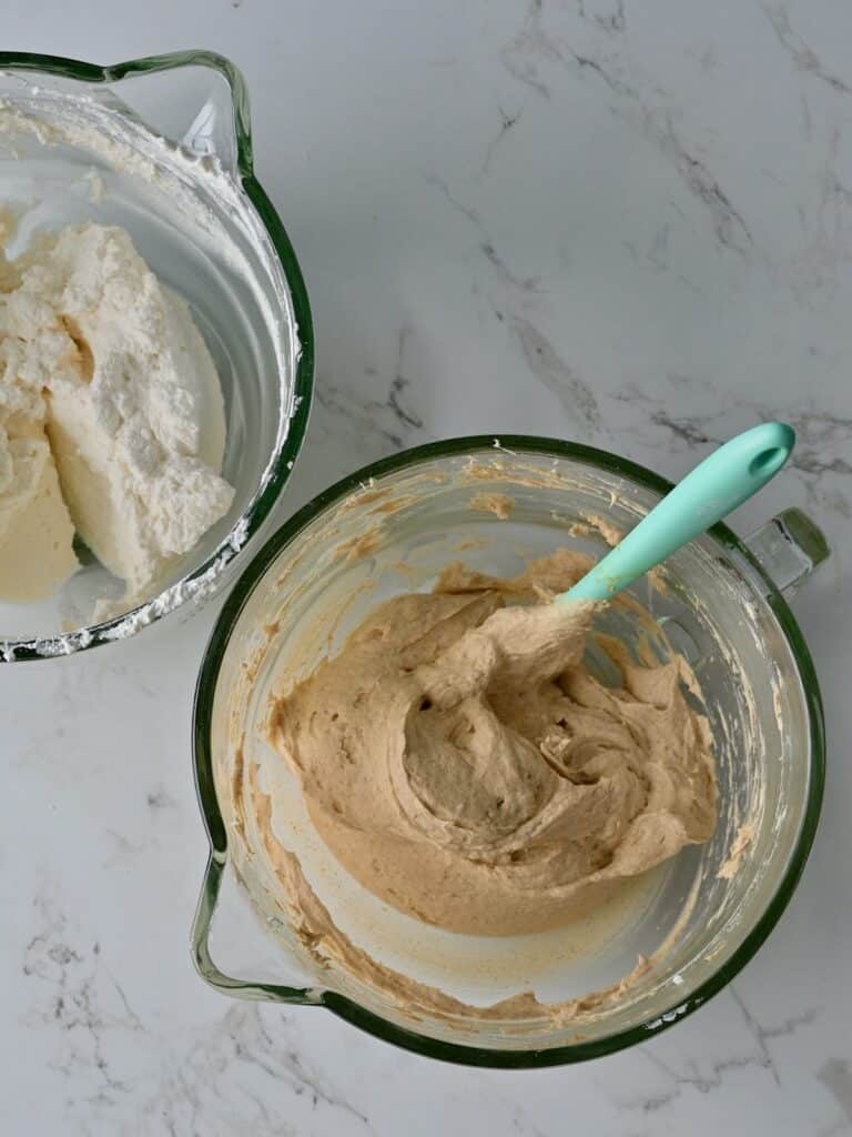A bowl of pumpkin mousse after whipped cream being gently folded into the mixture, and a bowl of whipped cream.