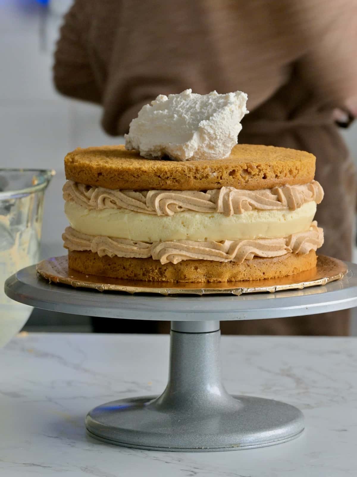 Pumpkin cake cheesecake being assembled with two pumpkin spice cake layers, a cheesecake center, and piped pumpkin mousse filling between each layer.