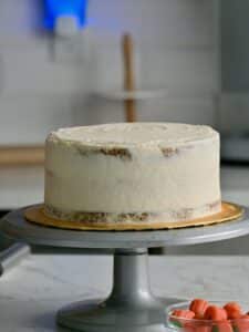 The assembled pumpkin cake cheesecake on a turntable, covered in a smooth, light layer of whipped cream frosting for a semi-naked finish.