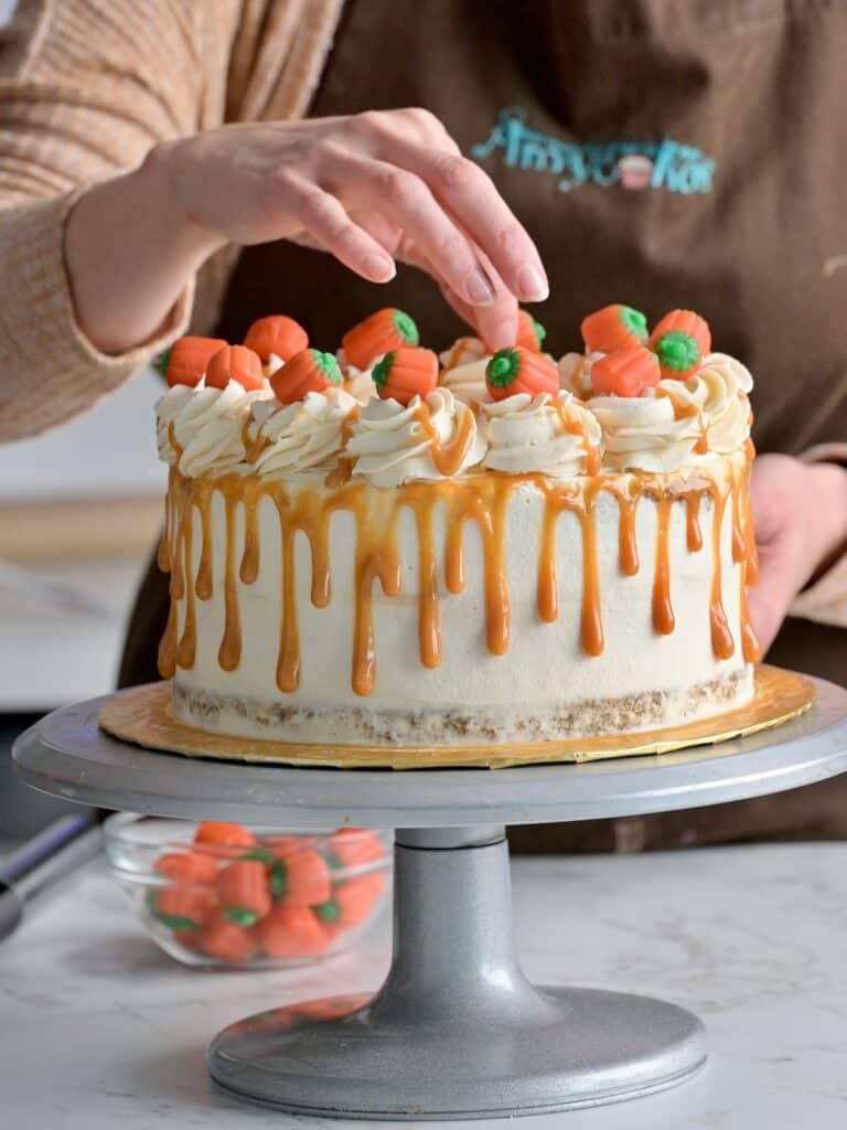 Candy pumpkins being placed on top of a finished pumpkin cheesecake layer cake.