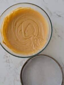 Pumpkin cake batter being whisked until smooth and creamy in a glass bowl, with a parchment-lined cake pan ready for baking.