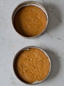 Two freshly baked pumpkin cake layers cooling in their pans.