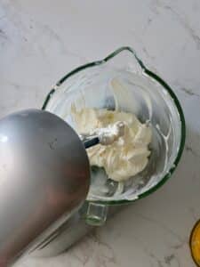 Cream cheese being blended with sugar in a stand mixer until smooth and creamy for the cheesecake layer of the pumpkin cake cheesecake.