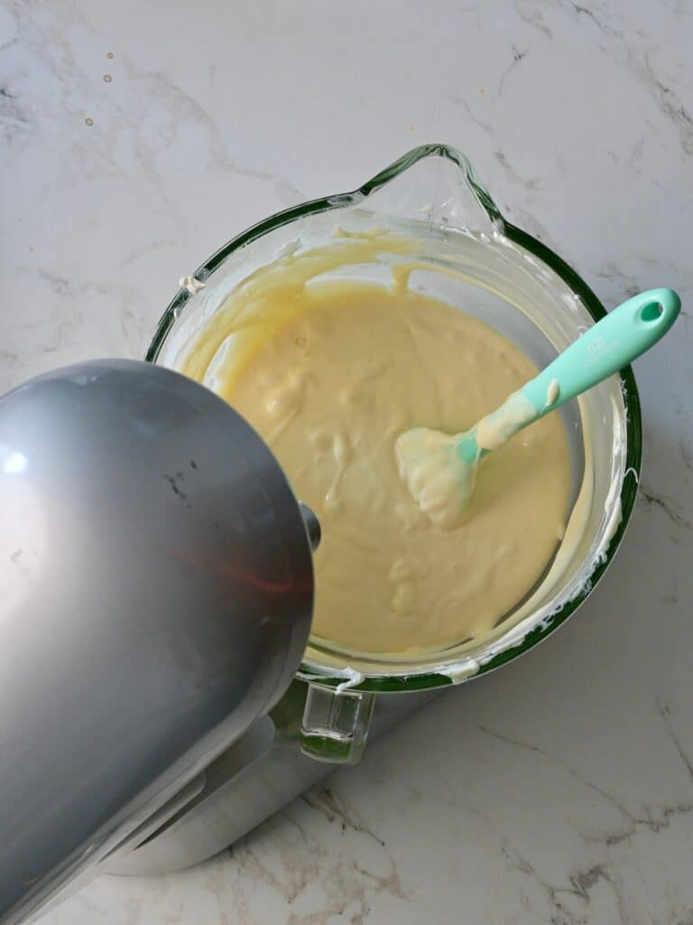 A mixing bowl filled with creamy cheesecake batter after adding eggs, vanilla, and heavy cream, ready to be poured into the pan.