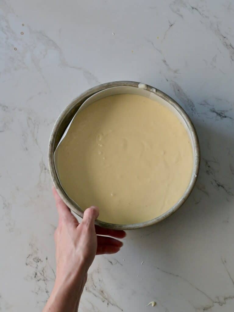 Smooth cheesecake batter poured evenly into a parchment-lined cake pan, ready to bake for the pumpkin cake cheesecake.