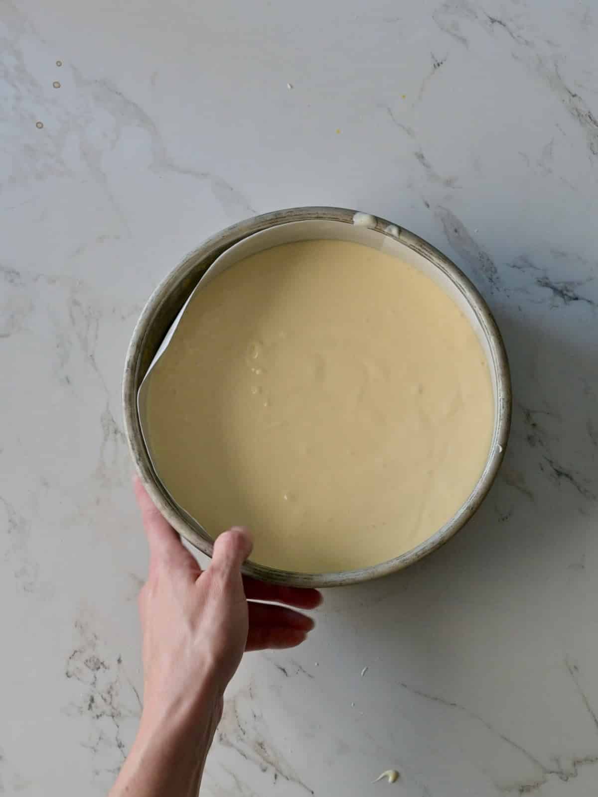 Smooth cheesecake batter poured evenly into a parchment-lined cake pan, ready to bake for the pumpkin cake cheesecake.