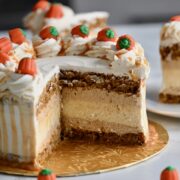 A close-up of a festive pumpkin cake cheesecake layer cake decorated with caramel-drizzled whipped cream swirls and candy pumpkins on top.