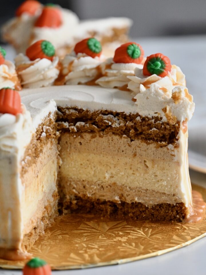 A close-up of a festive pumpkin cake cheesecake layer cake decorated with caramel-drizzled whipped cream swirls and candy pumpkins on top.