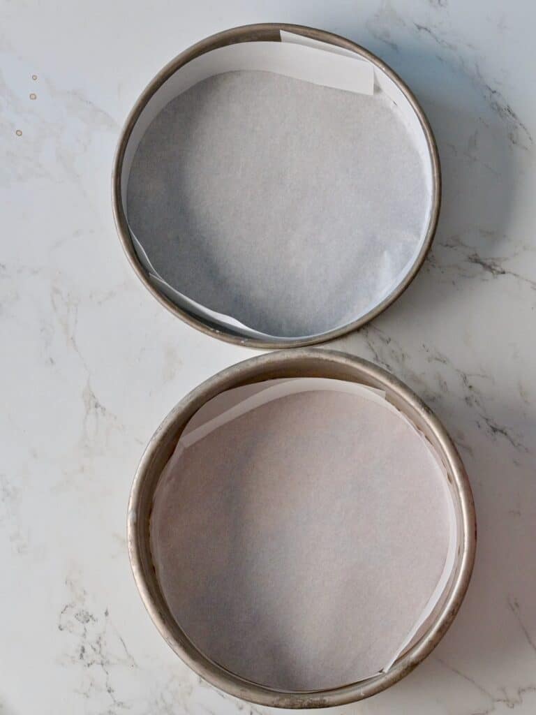 Parchment paper lining the two cake pans for the pumpkin cake layers.
