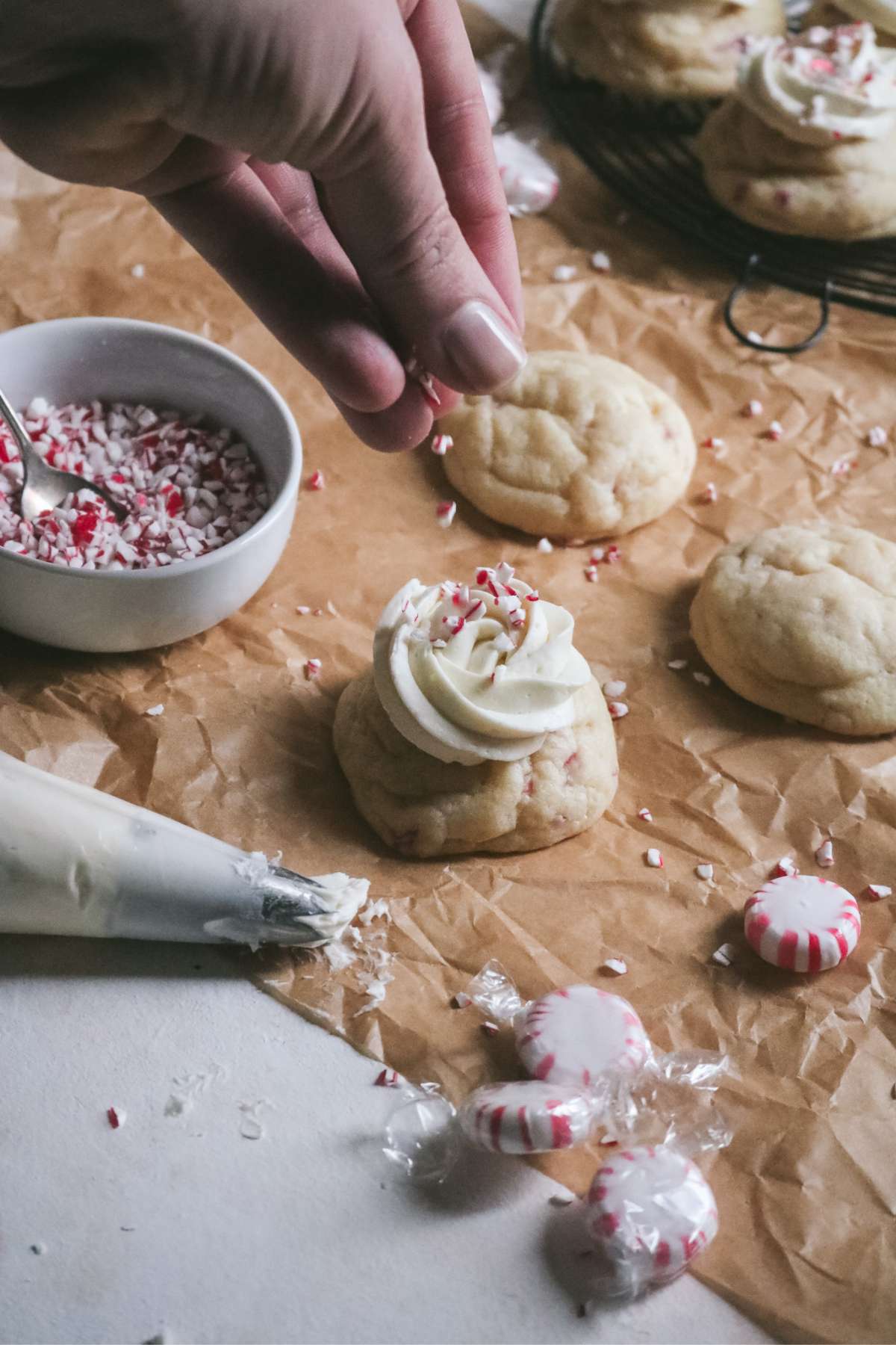 sprinkling crushed candy cane pieces on top of a frosted peppermint sugar cookie.
