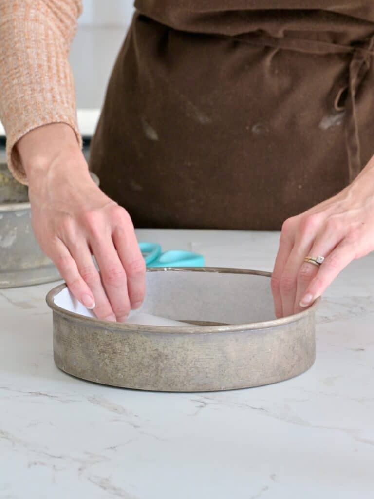 parchment paper lining the round cake pan for the cheesecake.