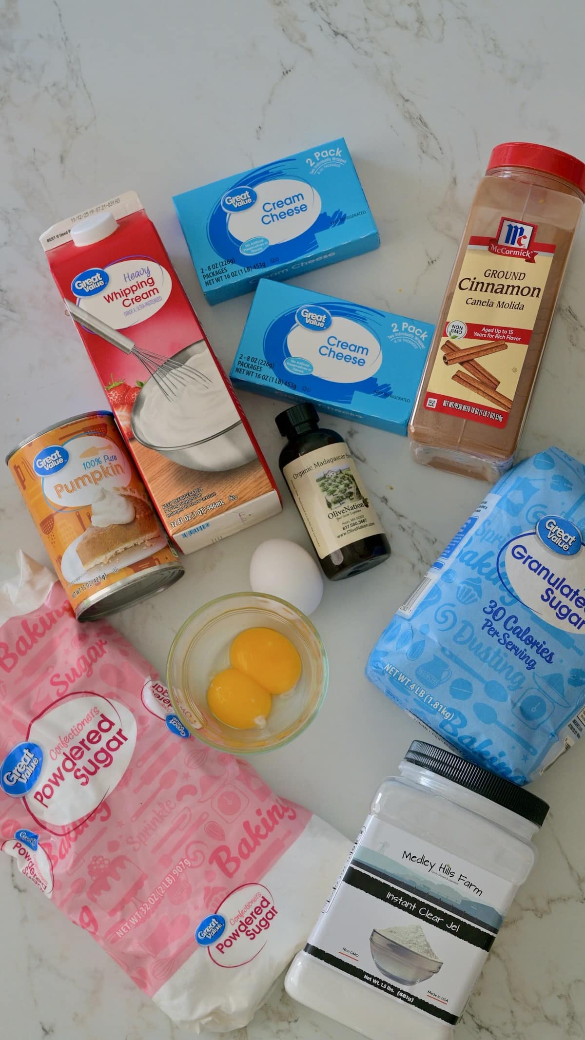 Ingredients for the cheesecake and the pumpkin cream cheese mousse and whipped cream, including cream cheese, heavy whipping cream, powdered sugar, canned pumpkin, eggs, vanilla, and cinnamon on a marble countertop.