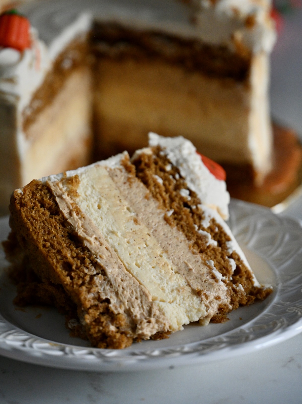 A close-up of a thick slice of pumpkin cake cheesecake showing moist cake and cheesecake layers with whipped frosting and caramel drizzle.