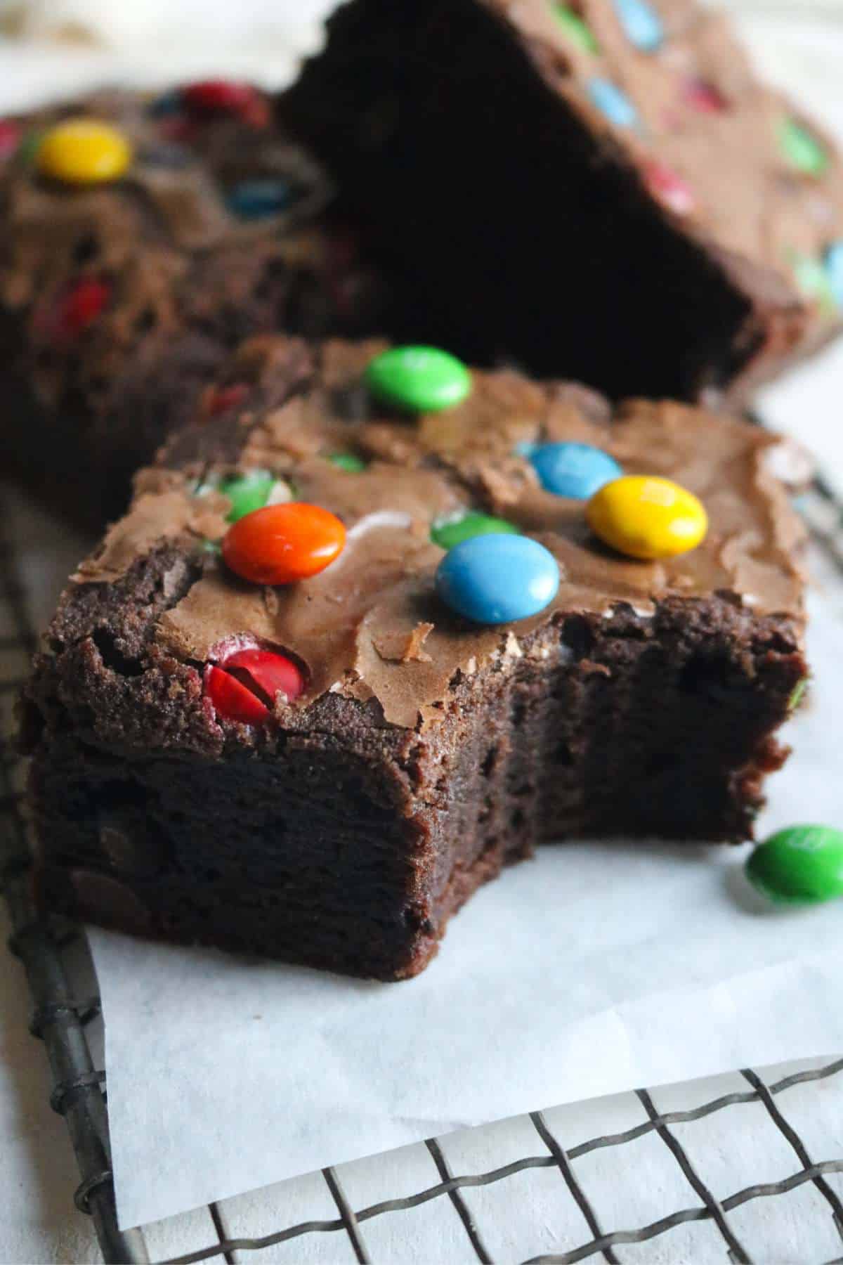 close up view of a thick brownie studded with m&ms with more brownies shingled in the background.