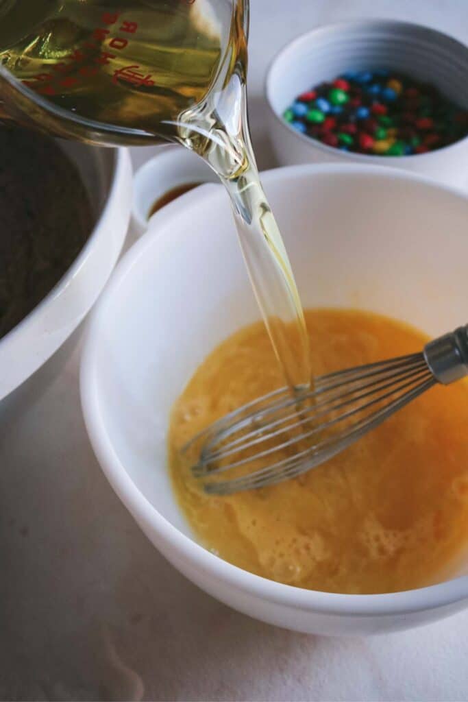 adding vegetable oil to whisked eggs for moist m&m brownies.