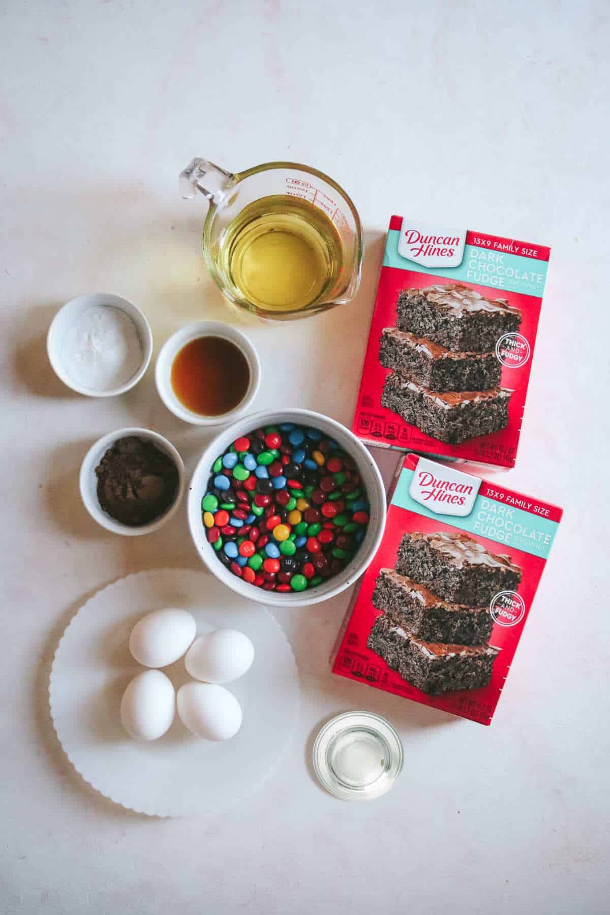 overhead view of all the ingredients to make fudgy m&m brownies including water, oil, brownie mix, eggs, and more.