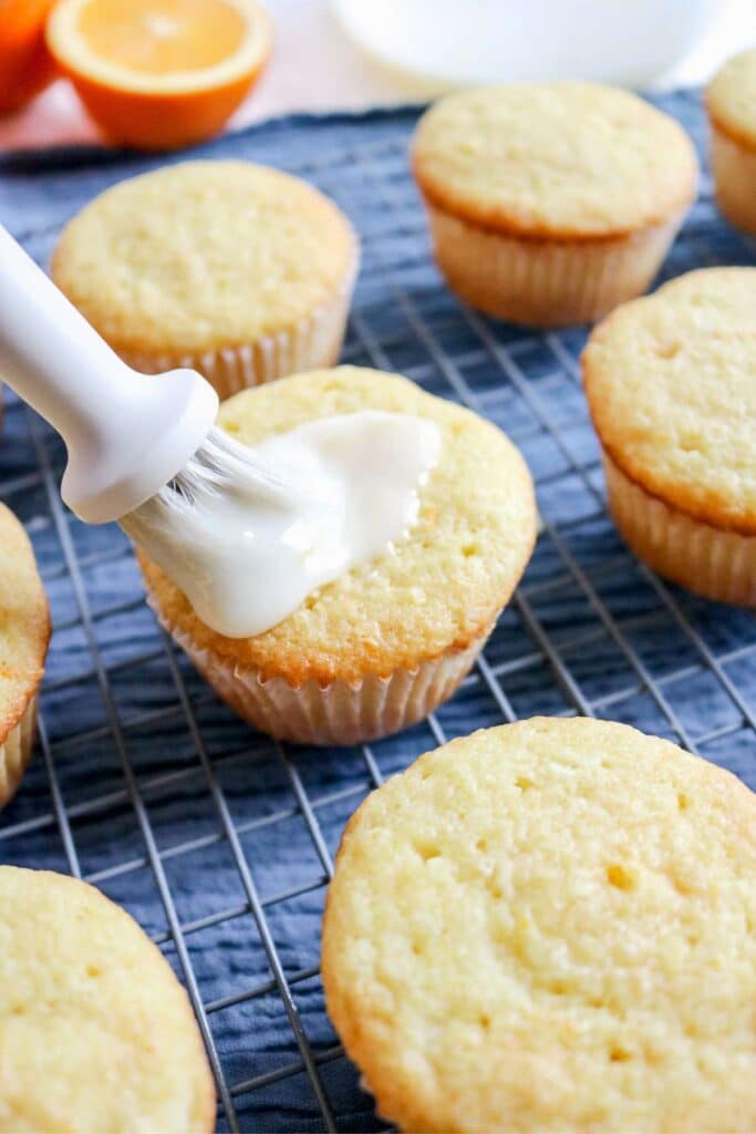 glazing orange cupcakes with a pastry brush.