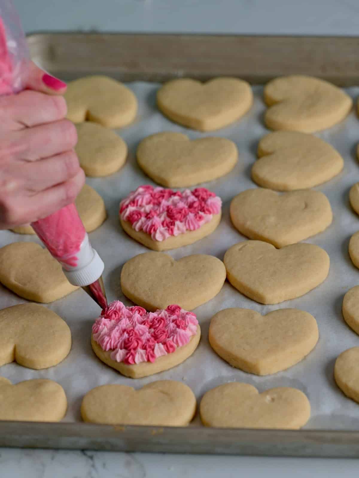 Heart cookies being piped with buttercream frosting in shades of pink.