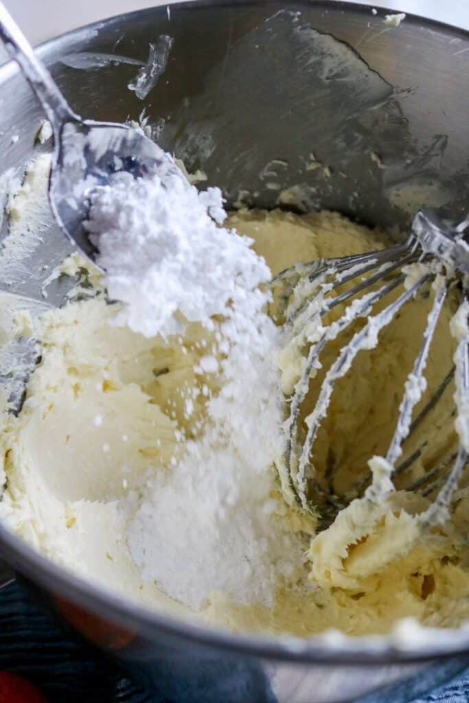 adding powdered sugar to mixing bowl with cream cheese, butter, and shortening for homemade frosting.