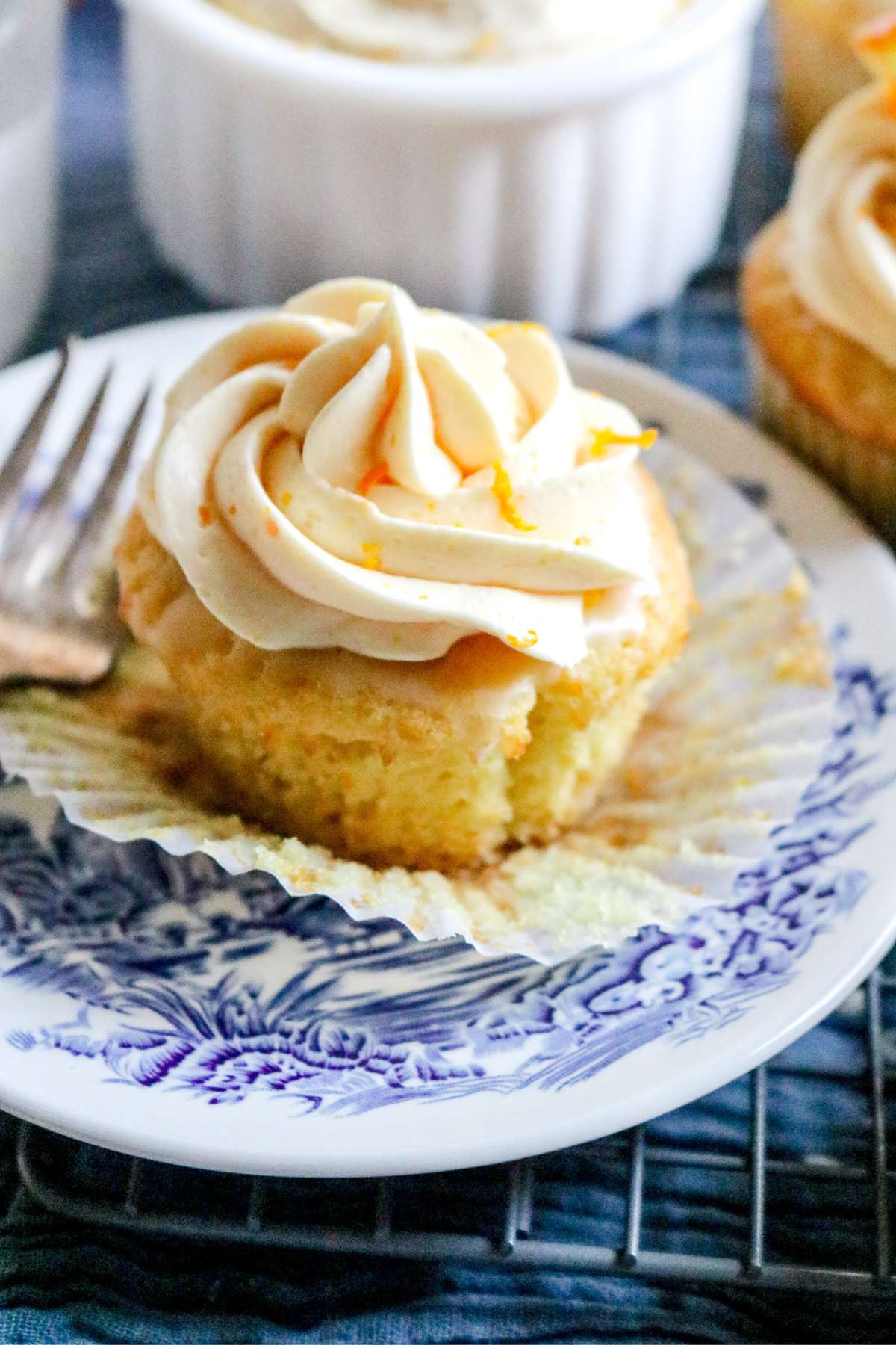 close up view of super soft homemade orange cupcakes in a paper liner on a blue and white plate.