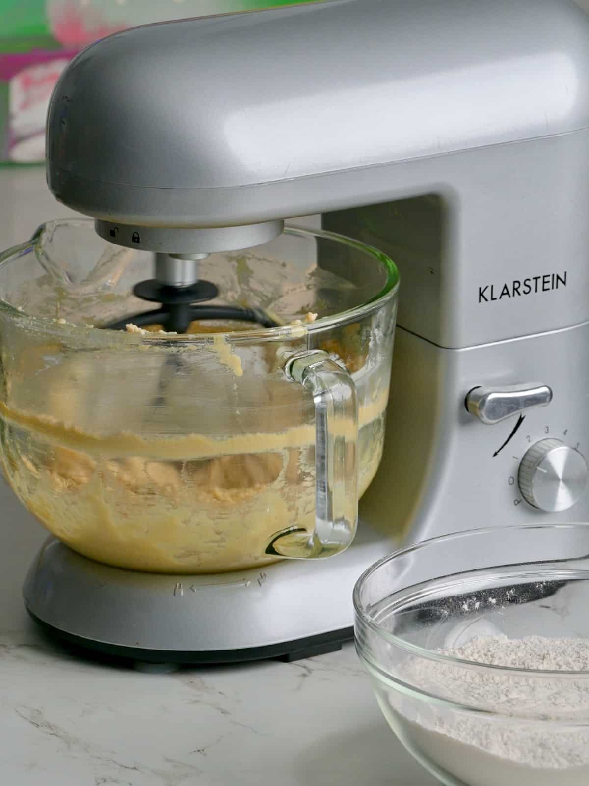Sugar cookie dough being made in a stand mixer, with dry ingredients in a bowl nearby.