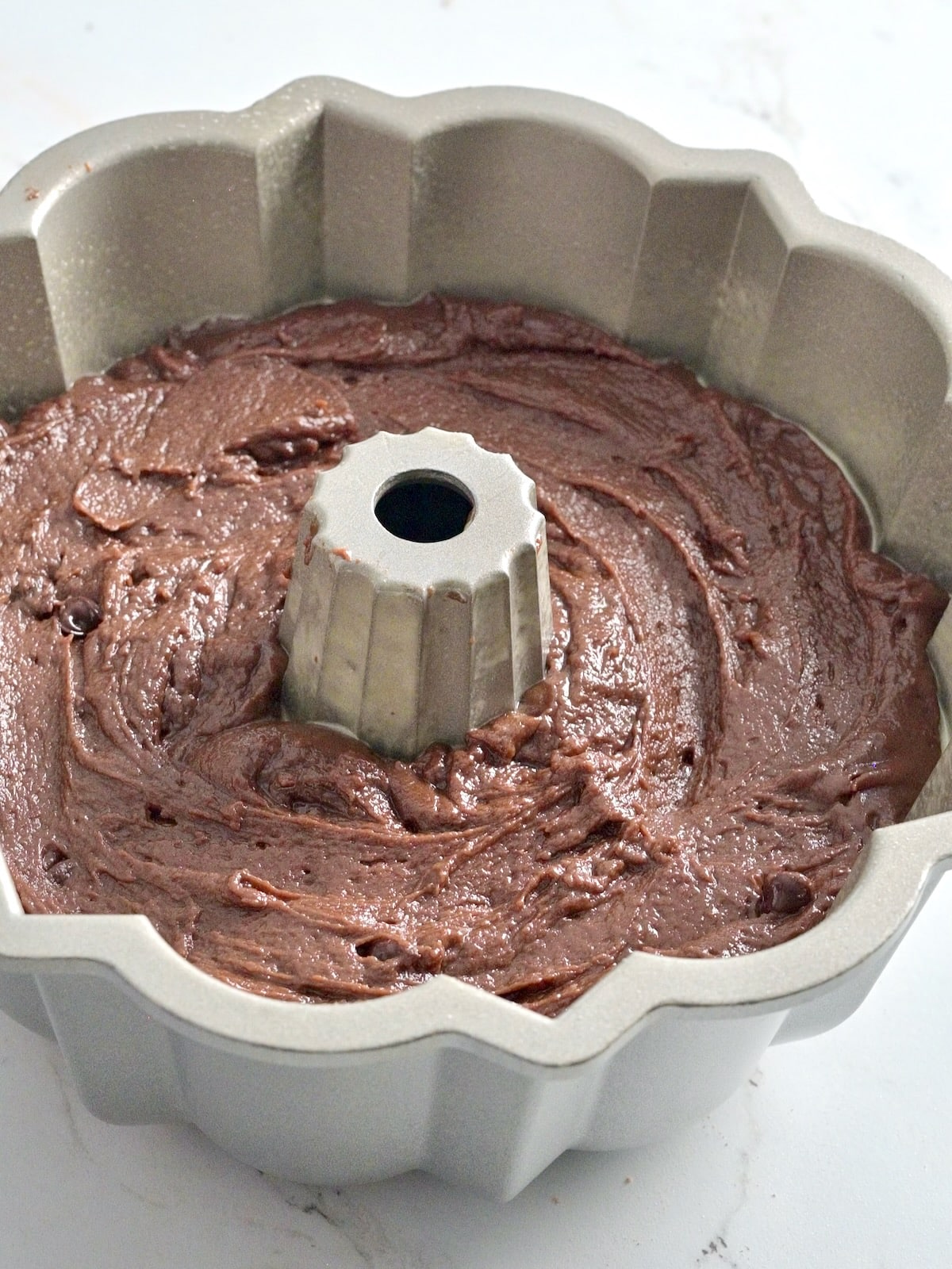 Chocolate bundt cake batter smoothed into a light silver Nordic Ware bundt pan before baking.