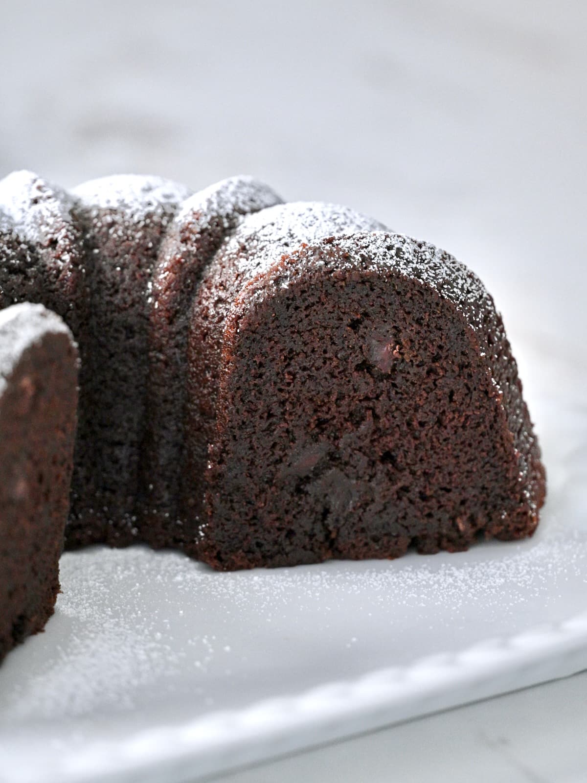 Sliced chocolate bundt cake showing moist crumb and melted chocolate chips, dusted with powdered sugar.