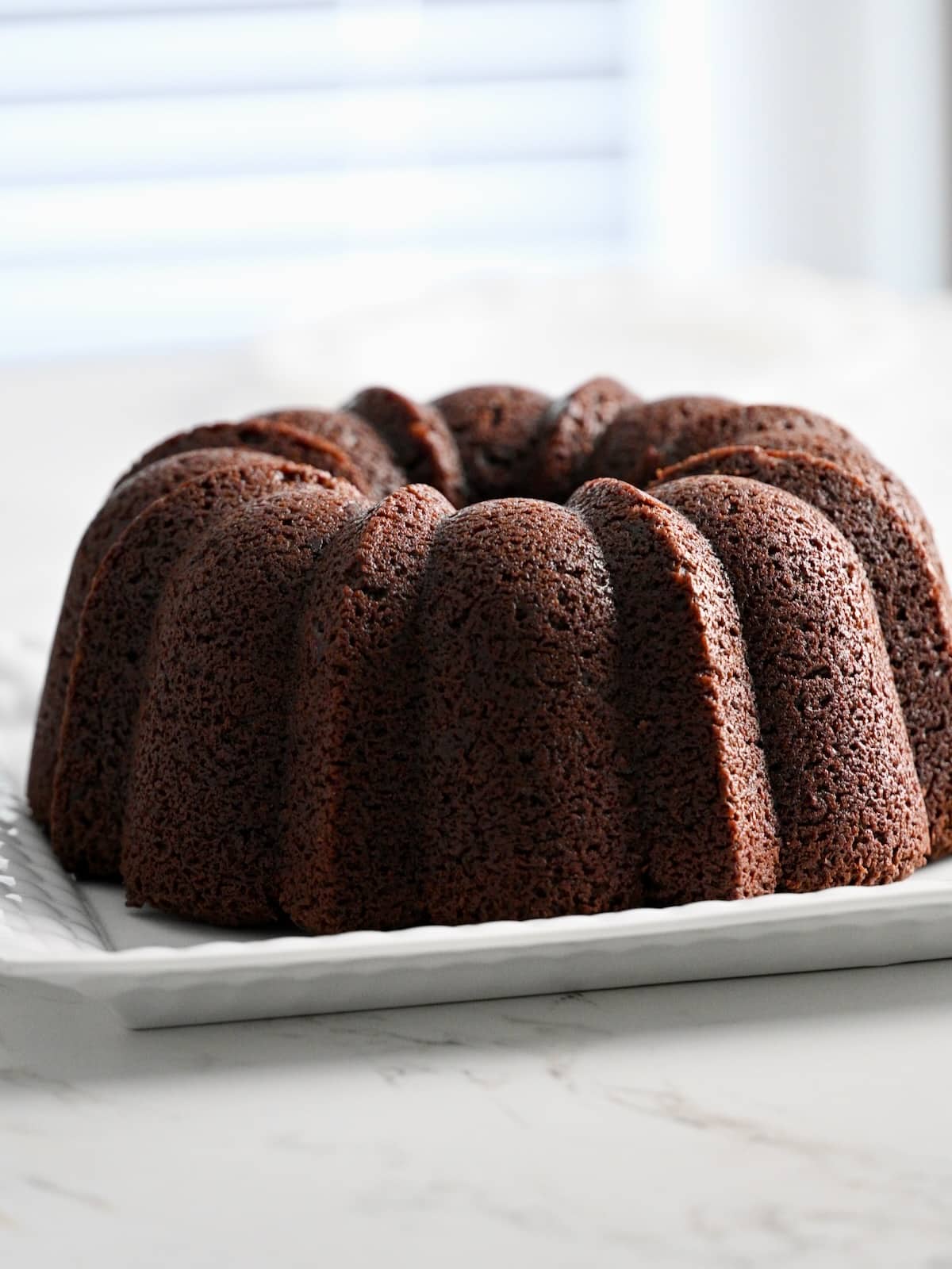 Whole baked chocolate bundt cake with defined ridges resting on a white platter.
