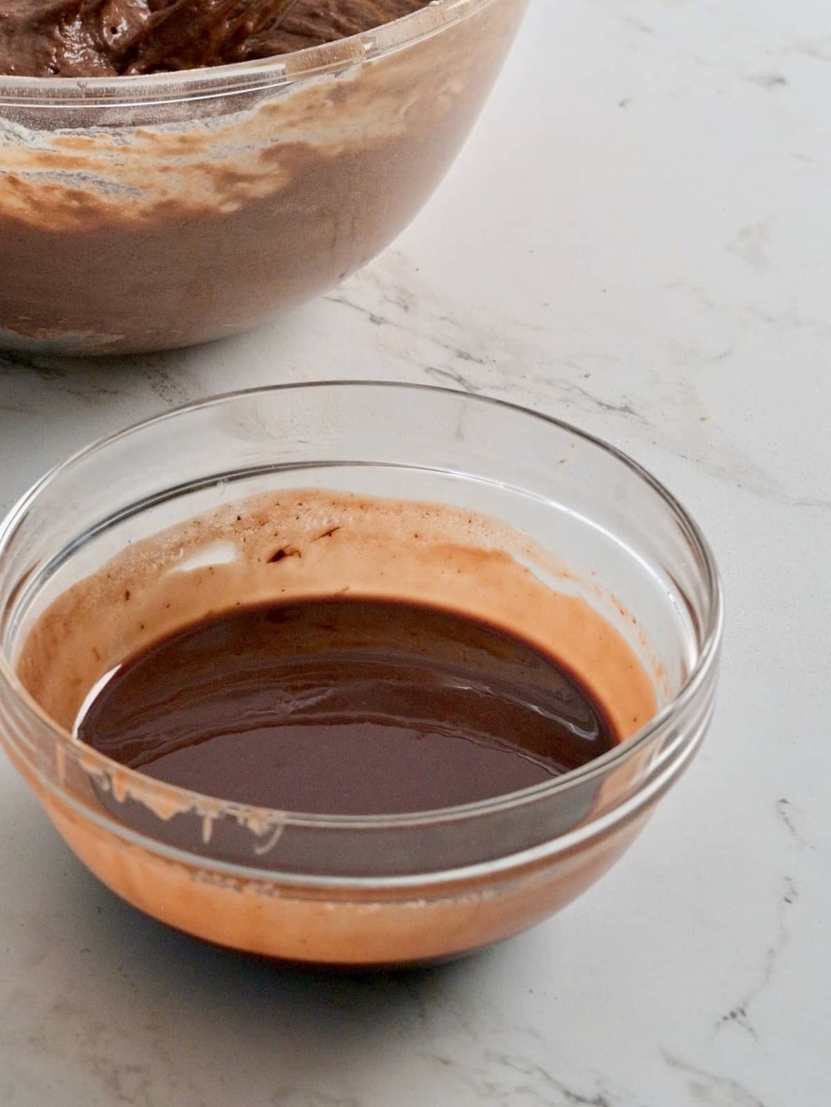Small glass bowl of smooth melted butter and chocolate chips next to chocolate bundt cake batter.
