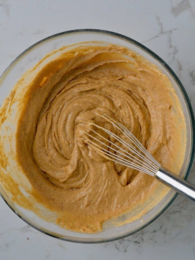Smooth, thick pumpkin spice cake batter in a glass bowl with a whisk.