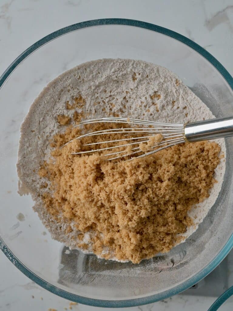 Brown sugar being whisked into flour and spices in a glass bowl for pumpkin mini bundt cake batter.