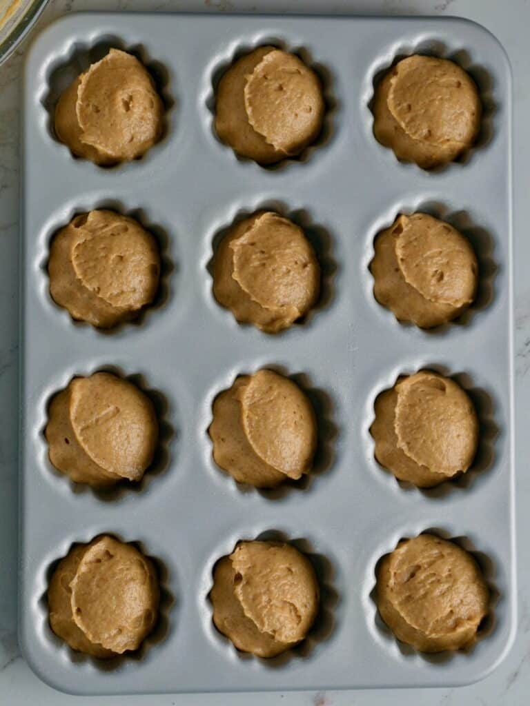 Scoops of pumpkin cake batter in the fluted wells of a mini bundt pan, ready for the oven.