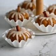 Glazed pumpkin mini bundt cakes in white fluted baking cups on a marble counter.