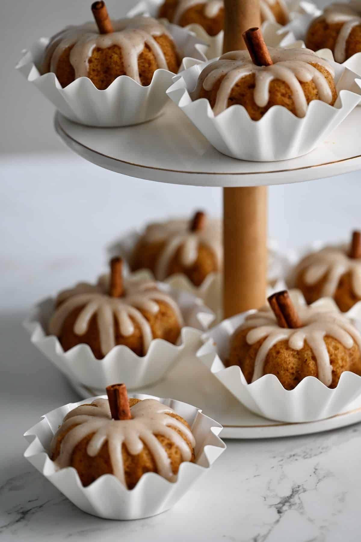 Pumpkin mini bundt cakes with cinnamon stick stems arranged on a two tier dessert stand.